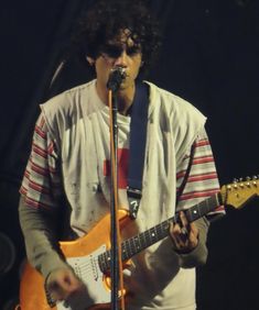 a man holding a guitar and singing into a microphone