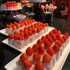 several desserts are arranged on white trays with strawberries in the middle, and candy sticks sticking out of them