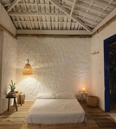 a white bed sitting under a wooden ceiling next to a blue door in a room