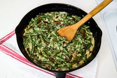 a skillet filled with green beans and bacon on top of a white countertop