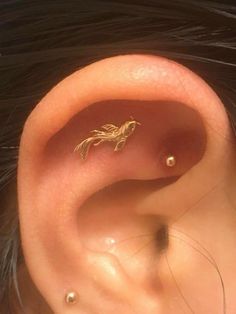 a close up of a person's ear with a small gold bird on it