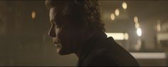 a man with curly hair looking off into the distance in a dimly lit room at night