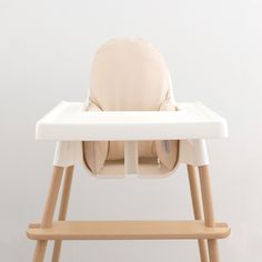 a white high chair with wooden legs and a beige seat cover on it's back