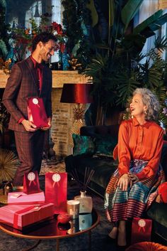 a man and woman standing next to each other in a living room filled with presents