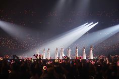 a group of women standing on top of a stage with lights in the dark behind them