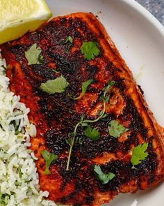 a white plate topped with meat and rice covered in cilantro next to a lemon wedge