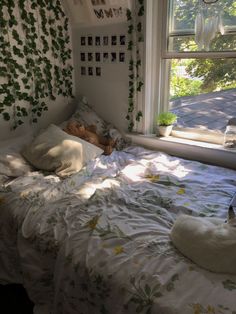 an unmade bed in front of a window with ivy growing on the wall behind it