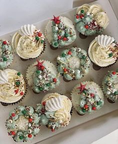 twelve cupcakes decorated with white frosting and christmas decorations on a baking sheet