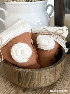 two brown felt houses sitting in a wooden bowl next to a white vase and candle