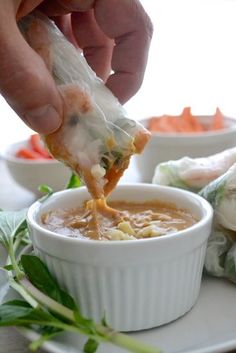 someone dipping some food into a small white bowl on top of a plate with carrots