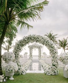 an outdoor wedding setup with white flowers and greenery on the grass, surrounded by palm trees