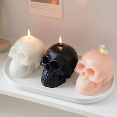 three candles that have been placed on a white tray with two skulls in the middle