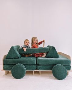 two children sitting on a green couch with wheels