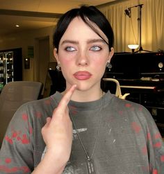 a woman with short black hair and blue eyes is holding her finger to her lips