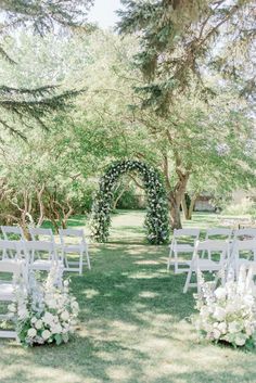 an outdoor ceremony setup with white chairs and greenery