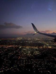 an airplane wing flying over the city lights at night with clouds in the sky above