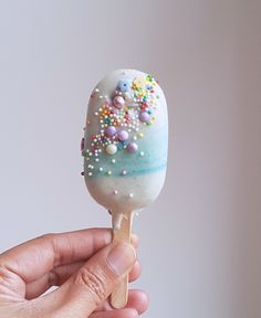 a hand holding a candy lollypop covered in sprinkles and candies