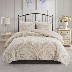 a bed with white comforter and two pictures on the wall in front of it