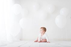 a baby sitting on the floor in front of balloons