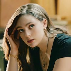 a beautiful young woman sitting down with her hand on her head and looking at the camera