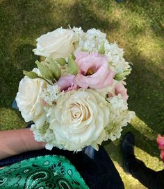 a person holding a bouquet of white and pink flowers in their hand on the grass