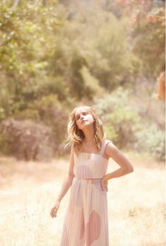 a girl in a pink dress is standing in the grass with her hands on her hips