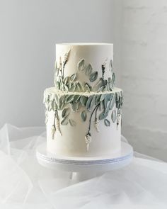 a three tiered white cake with green leaves on it