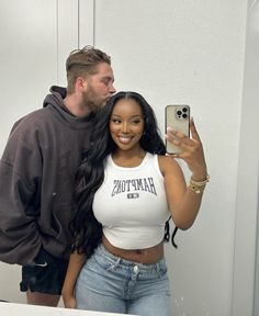 a man standing next to a woman taking a selfie in front of a mirror