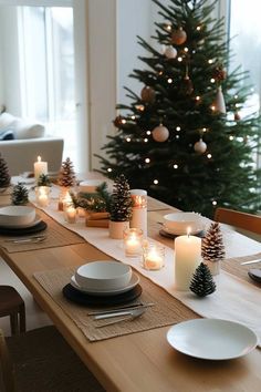 a dining room table set for christmas with lit candles and pine cones on the table