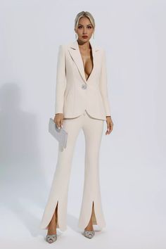 a woman in a white suit and heels standing on a white background with her hands behind her back