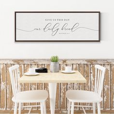 two white chairs at a table with a sign above it that says give us this day one calligraphy