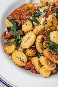 a white plate topped with gnocchini and spinach next to a fork