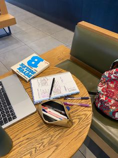 an open laptop computer sitting on top of a wooden table next to a book bag