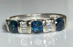 "Beautiful natural sapphire and diamond band in 14K white gold. This pretty ring features three sparkling natural blue sapphires and six tapered baguette diamonds. The band measures 4.2mm north to south at its widest and is in excellent, like-new condition. The sapphires measure 4.1mm each (about .26ct each) and the diamond baguettes measure about 2.4mm each. Total carat weight (diamond equivalent) is approximately .95ct. No visible chips or cracks under magnification. Ring size 7 and easily  sized up or down several sizes.  Please allow three business days for sizing. One month layaway payment plans on items $500 and over available. Approximate Age - vintage Gemstone(s) - natural sapphires and diamonds Metal - 14K white gold Weight - 3.35 grams Ring size - 7 Marks - 14K  Makers Mark -  Co Blue Diamond Ring With Baguette Diamonds, Blue Baguette Cut Diamond Ring With Baguette Diamonds, Blue Baguette Diamond Ring, Blue Diamond Ring With Baguette Diamonds For Anniversary, Anniversary Blue Diamond Ring With Baguette Diamonds, Diamond Baguette Band, Baguette Band, Baguette Diamond Band, Sapphire And Diamond Band