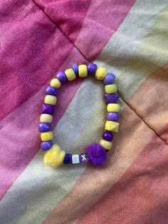 a purple and yellow beaded bracelet sitting on top of a pink striped blanket,