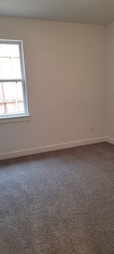 an empty room with a window and carpeted floor is shown in this image,