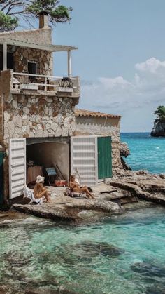 two dogs laying on the rocks in front of a house with an open door and green shutters