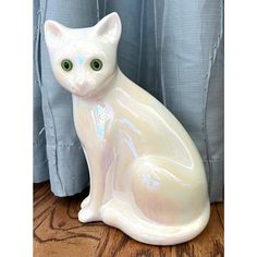 a white cat statue sitting on top of a wooden floor next to a blue curtain