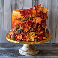 a cake decorated with autumn leaves and acorns on a stand in front of a wooden wall