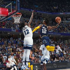 two men playing basketball in front of an audience at a sporting event, one jumping to dunk the ball