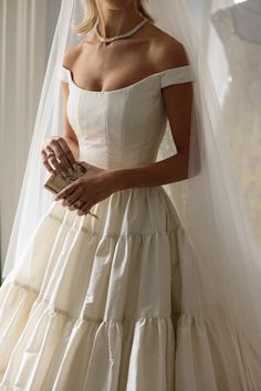 a woman in a wedding dress is holding a small purse and posing for the camera