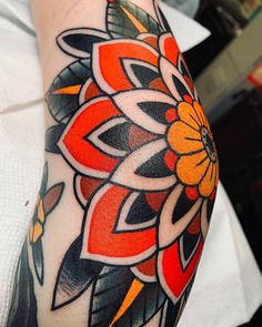 an orange and black flower tattoo on the arm