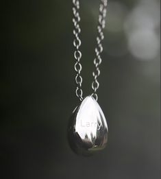 a silver necklace with a tear hanging from it's center and the word let on it