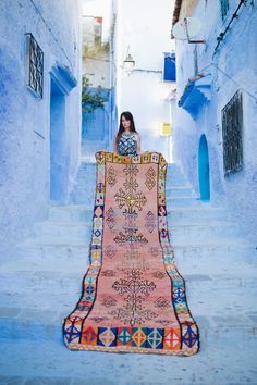 a woman standing in an alleyway with a rug on the ground and texting, save