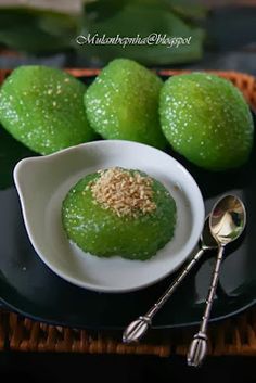 some limes are sitting on a black plate with silver spoons and two green lemons