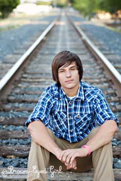 a young man is sitting on railroad tracks