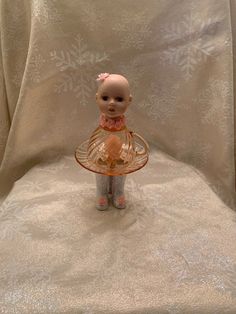 a small doll sitting on top of a chair with a glass plate in front of it