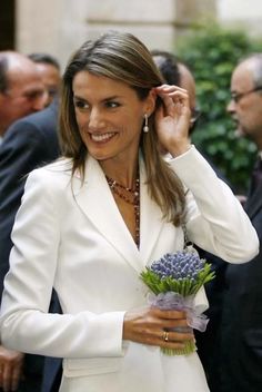 the woman is wearing a white suit and holding a purple flower in her left hand