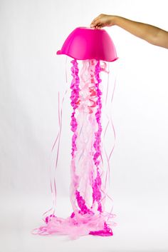 a pink jellyfish is being held up by a person's hand over a white background