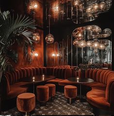 a room filled with lots of red couches and round tables surrounded by hanging lights